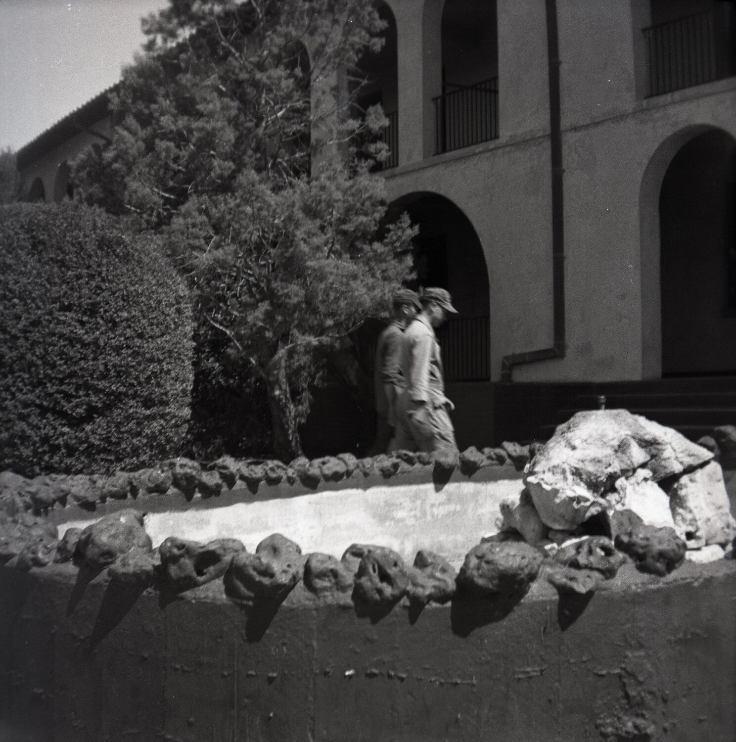 Two Airmen Walking Past Decorative Stone Wall, USAF Barracks Area