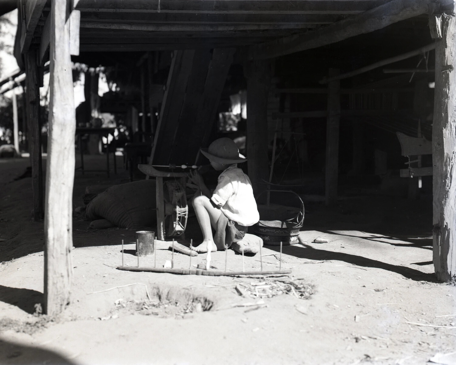 Villager Spinning Thread Beneath a Stilt House, China-Burma Region, WWII Era