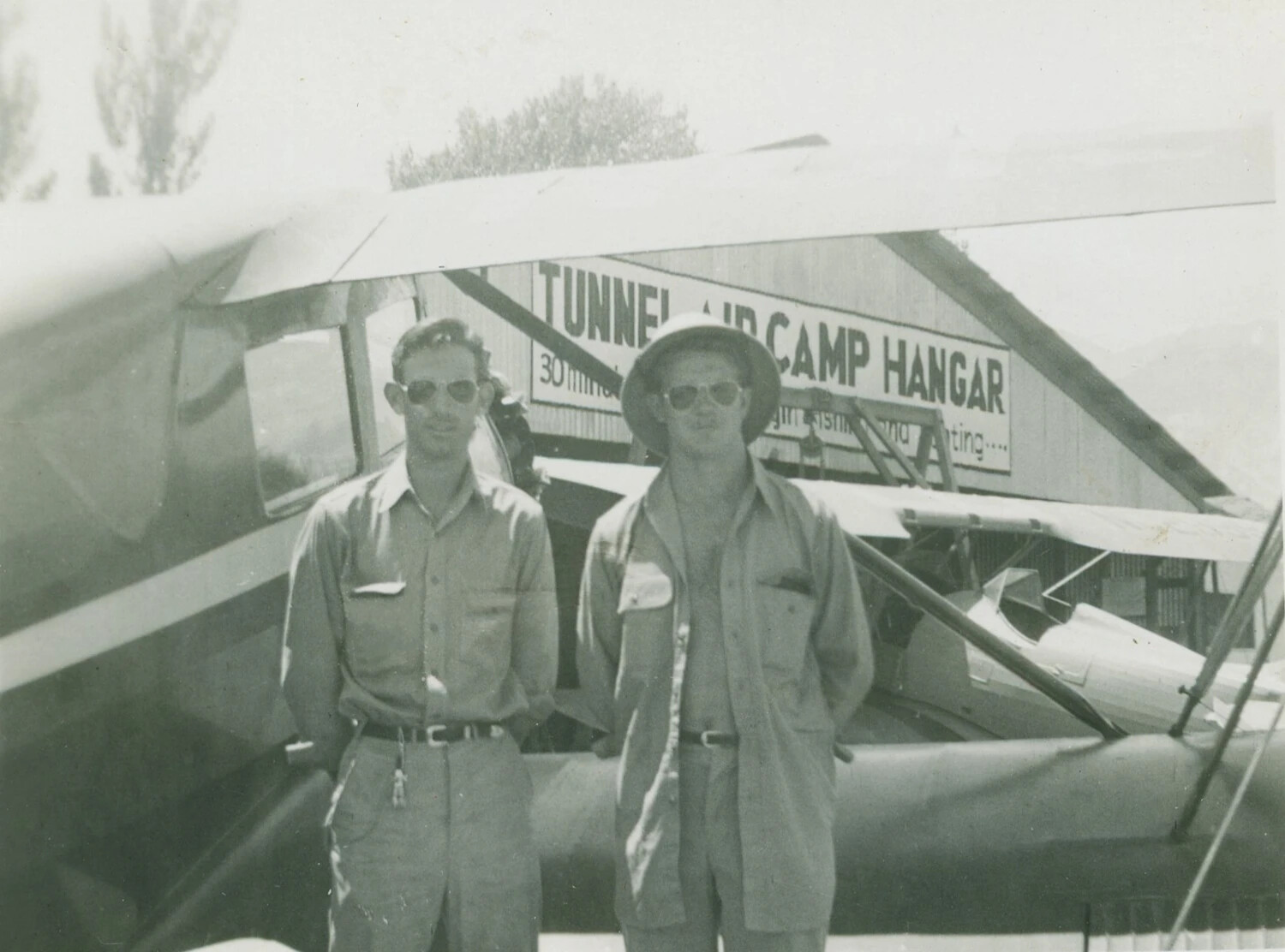 Two Men Before Light Aircraft at Tunnel Air Camp Hangar