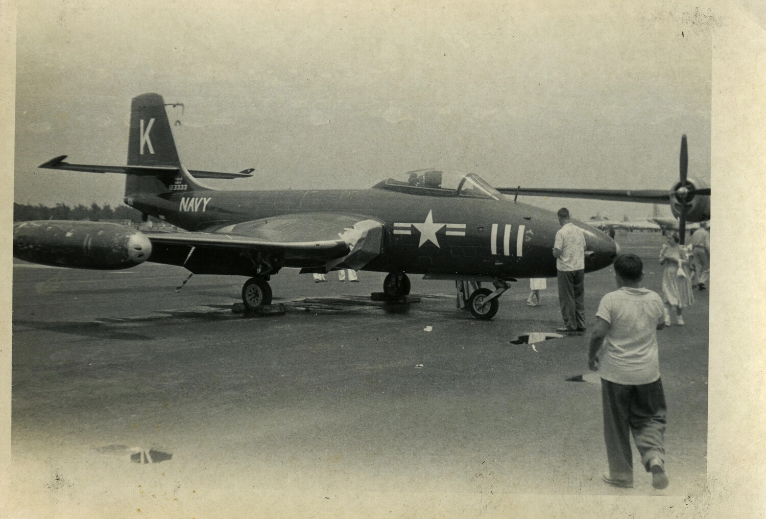 U.S. Navy Jet Fighter on Airfield Ramp with Civilian Onlookers, Early 1950s