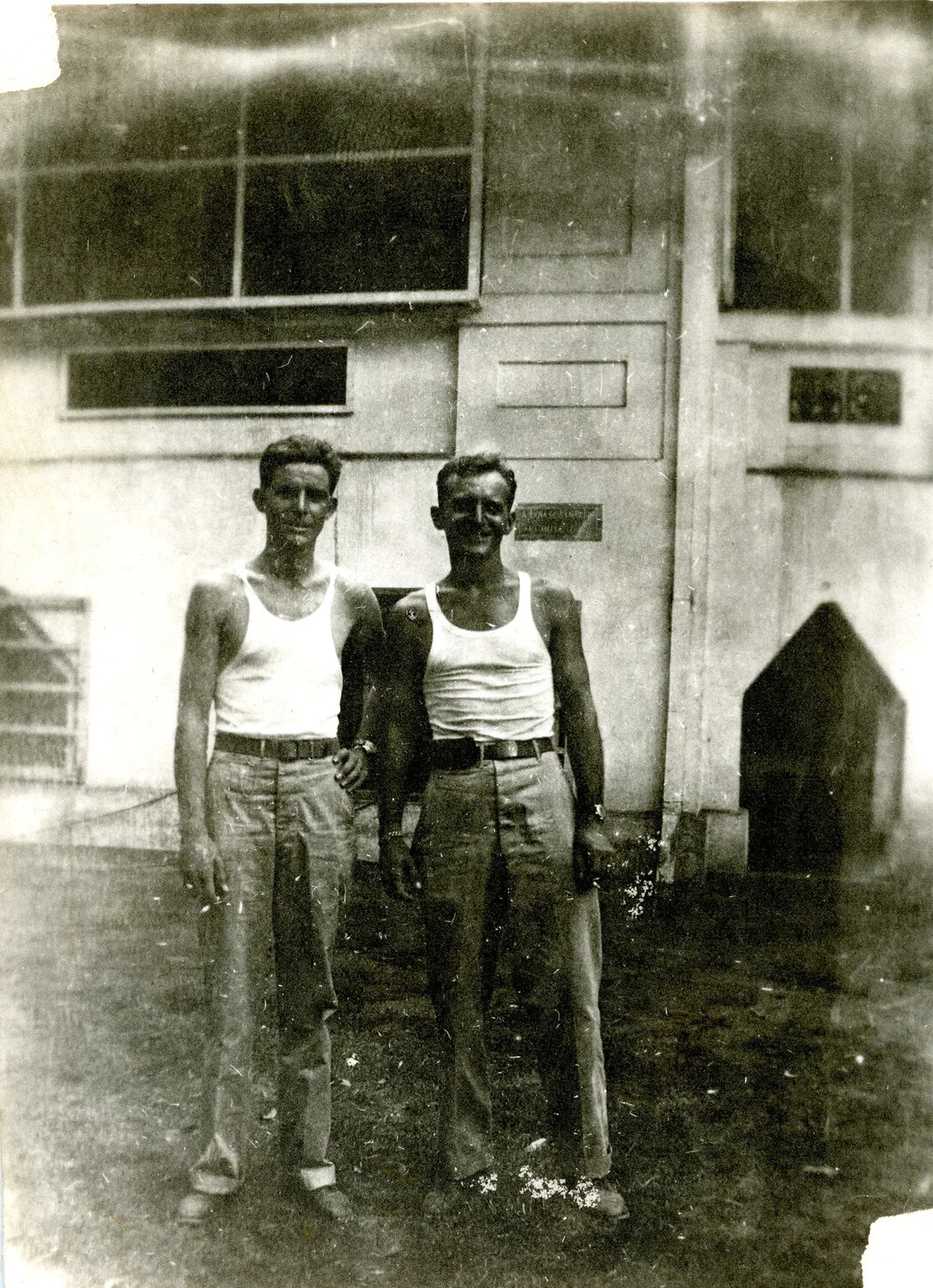 Two Servicemen in Undershirts Before Hangar or Warehouse Building, WWII-era Personal Photograph