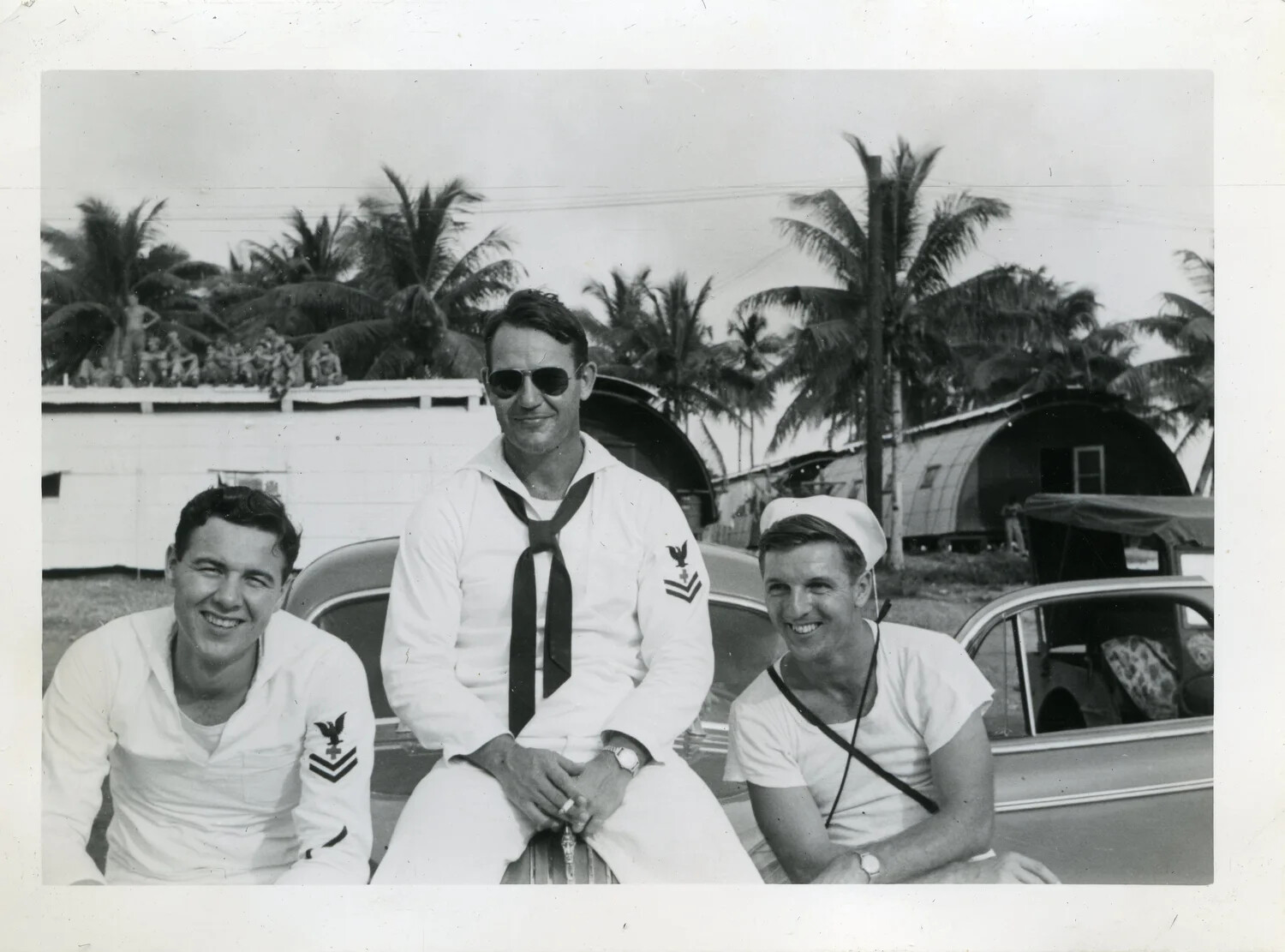 Three US Navy Petty Officers Seated on a Car, Quonset Huts and Palm Trees in Background -- VR-6 Naval Air Transport Squadron Album (Guam/Manila)
