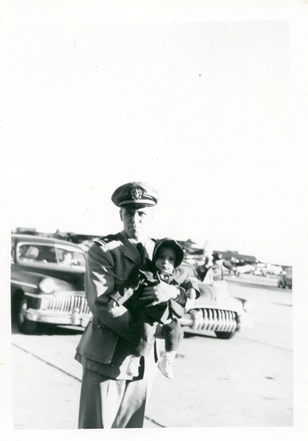 Naval Officer Holding a Young Child Beside Parked Automobiles, Early 1950s