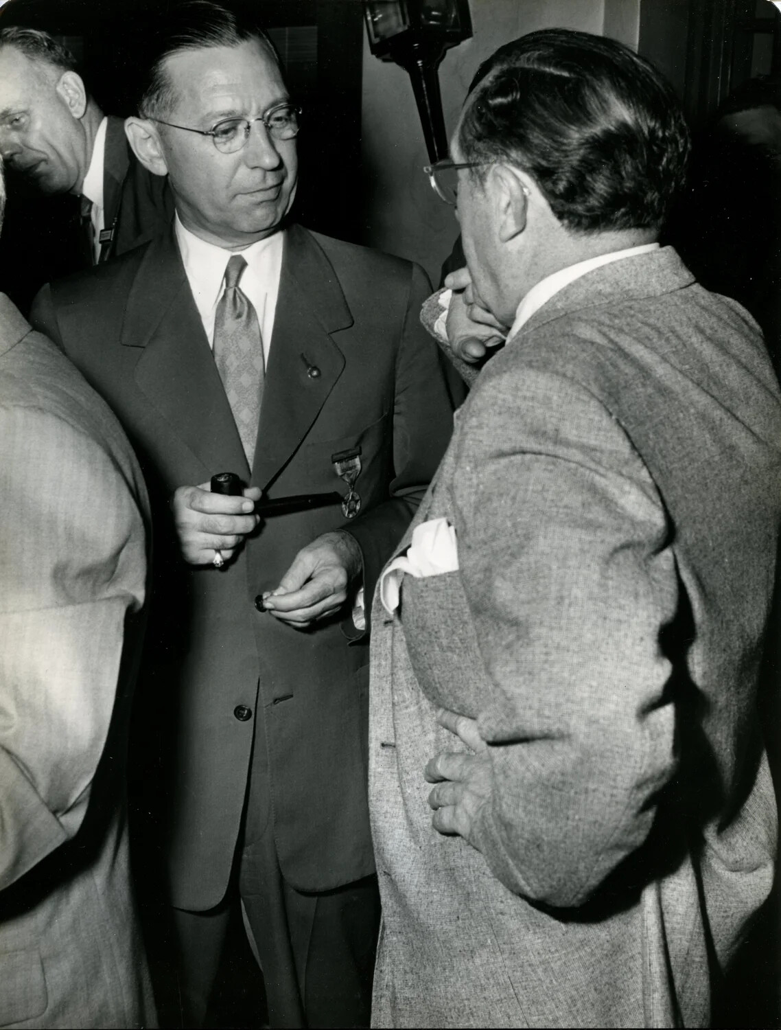 Attendee with Pipe and Lapel Medal Speaking with Tweed-Jacketed Figure, Late 1940s Convention