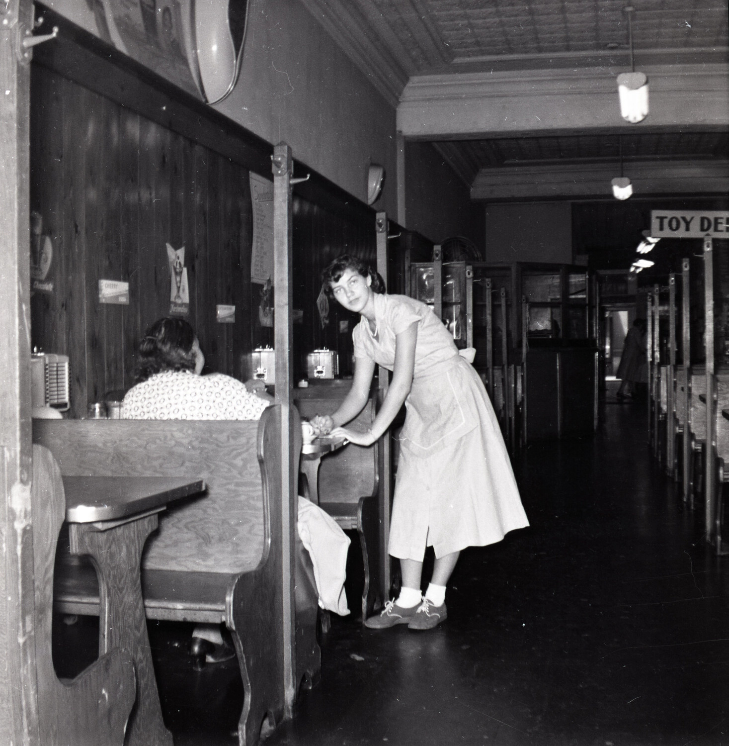 Waitress at Lunch Counter Booth in 1950s Variety Store, with Toy Department Signage