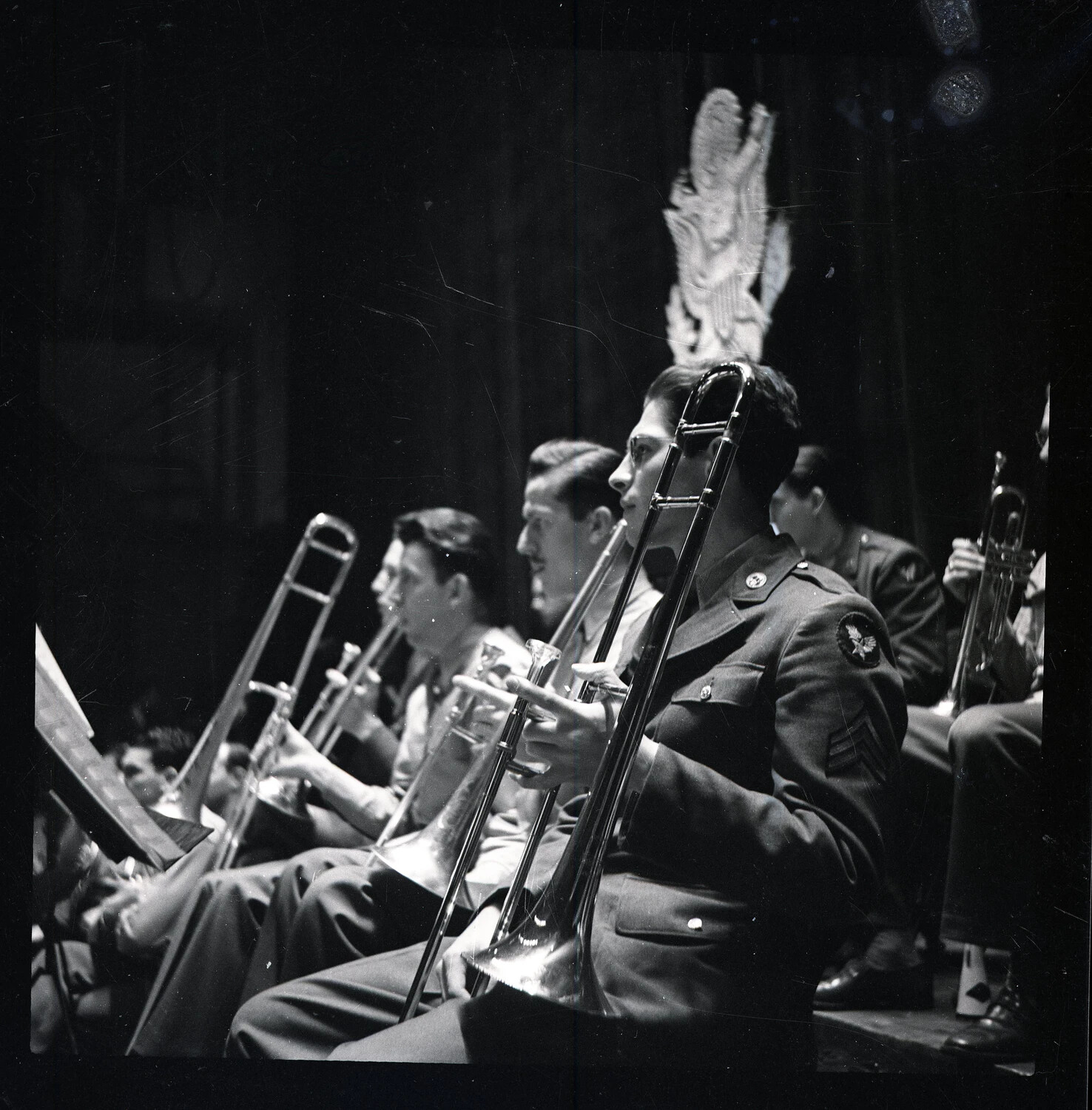 Trombone Section of a Military Band Performing on Stage Beneath an Eagle Emblem