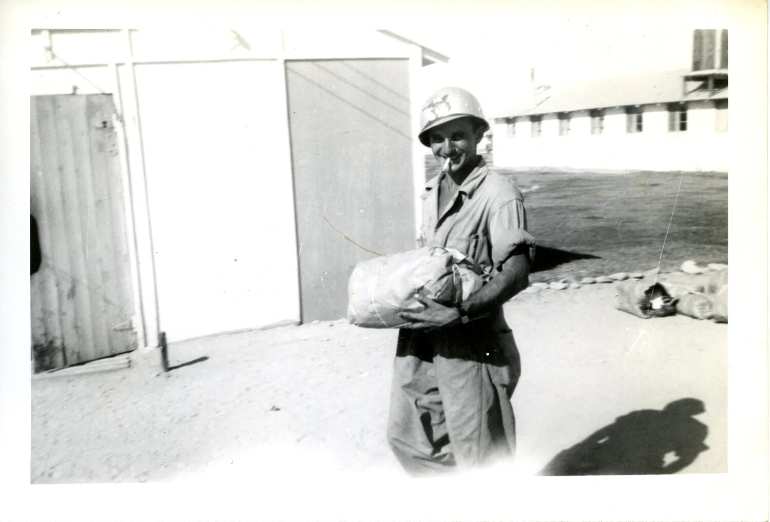 Serviceman in M1 Helmet Carrying a Bundled Sack at a Military Base