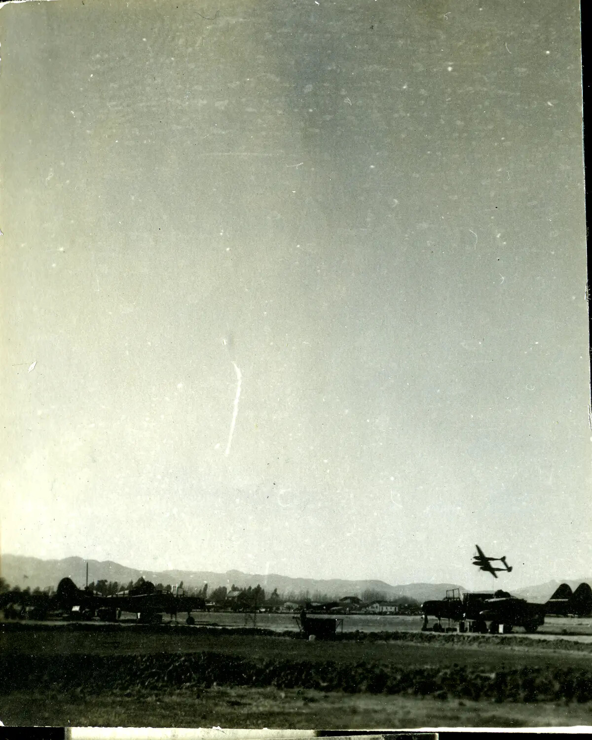 P-38 Lightning in Low Flight Over CBI Theater Airfield with Parked B-25 Mitchells