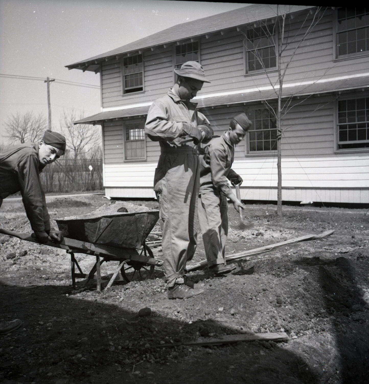 Servicemen Performing Grounds Work with Wheelbarrow Near Barracks