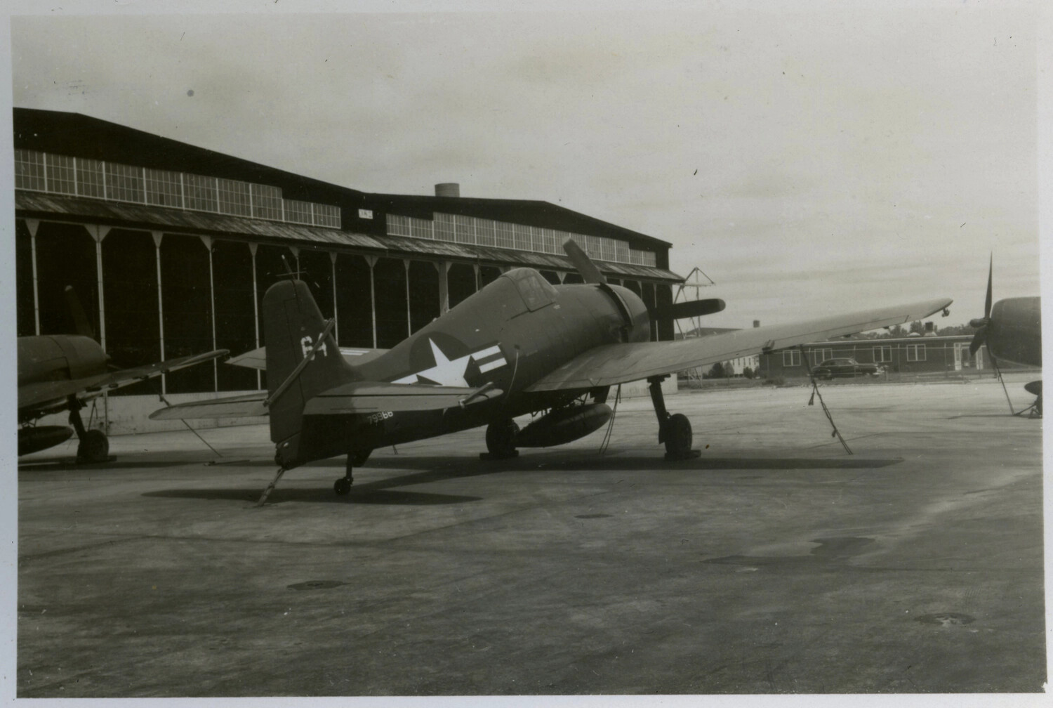 F4U Corsair Fighter Parked on Ramp Before Wooden Hangar, Naval Air Station