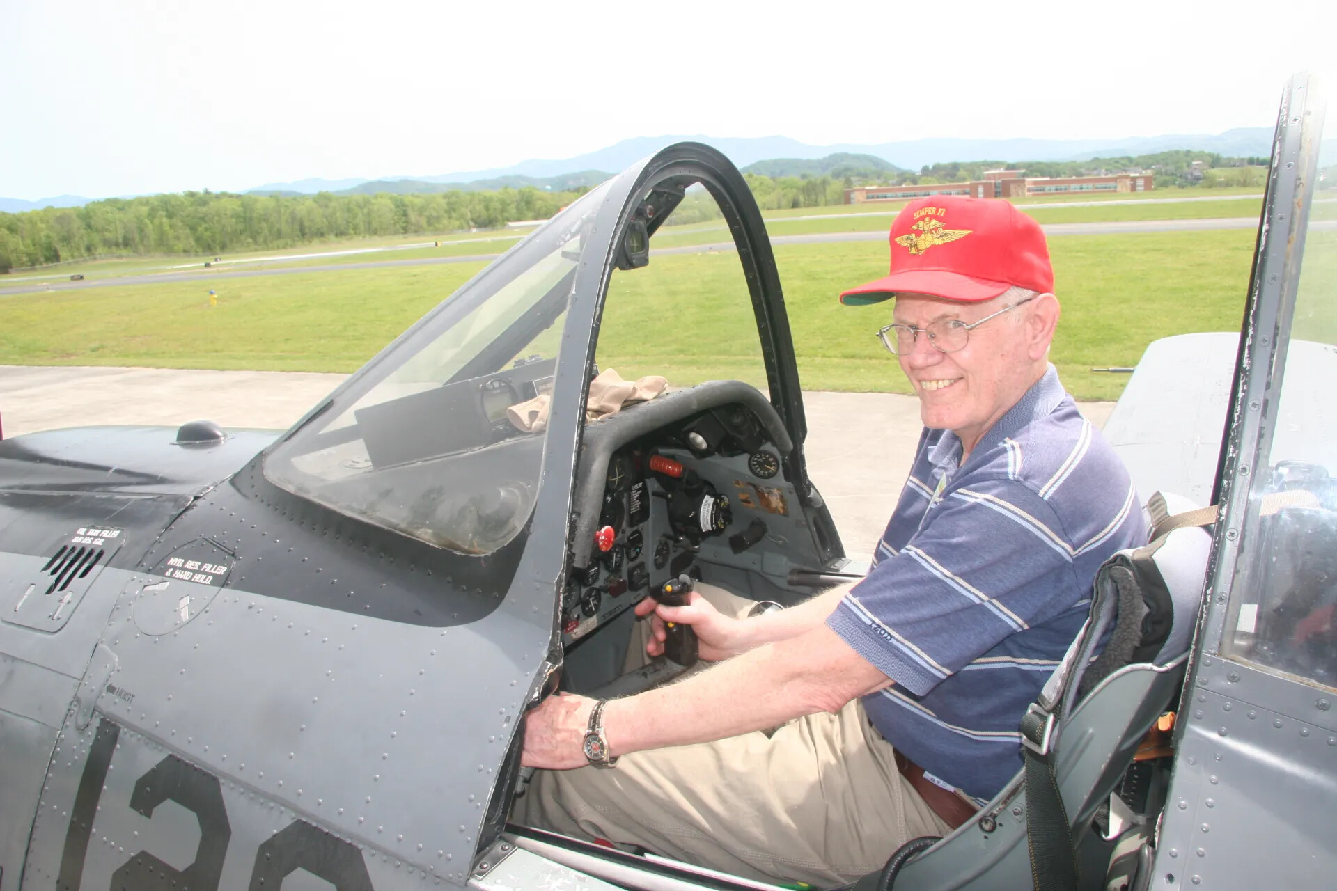 Attendee Smiling in Cockpit of T-28-Type Trainer Aircraft, "Semper Fi" Cap Visible