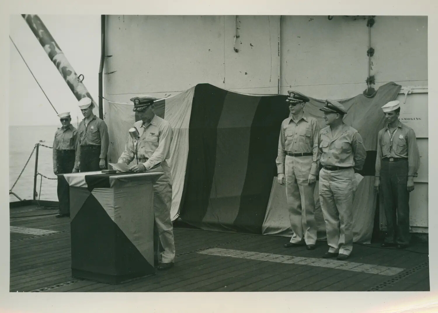 Shipboard Ceremony Aboard USS Petrof Bay (CVE-80), Officer Addressing Assembled Crew at Podium