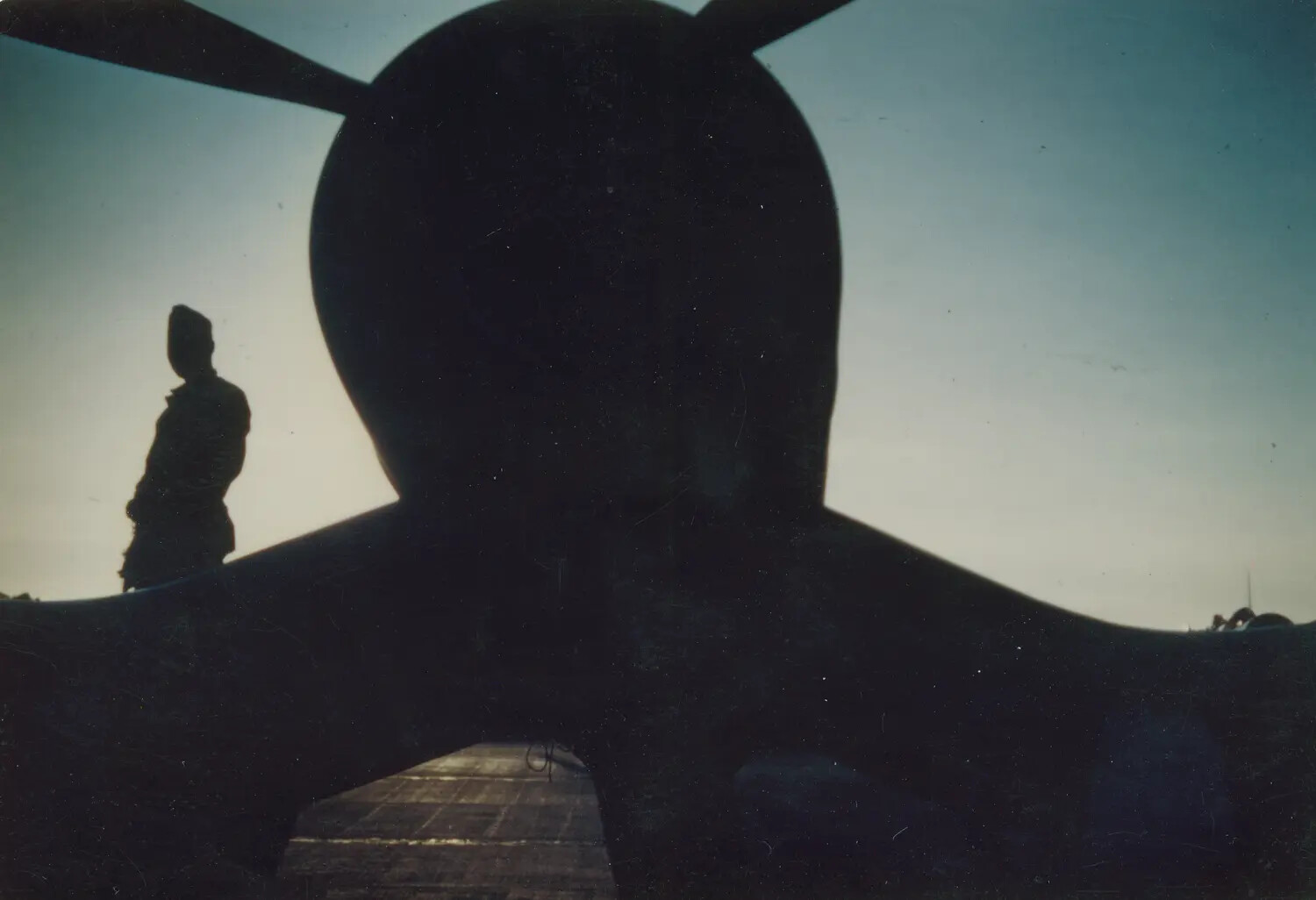 Silhouetted Carrier-Based Propeller Aircraft and Sailor at Dusk