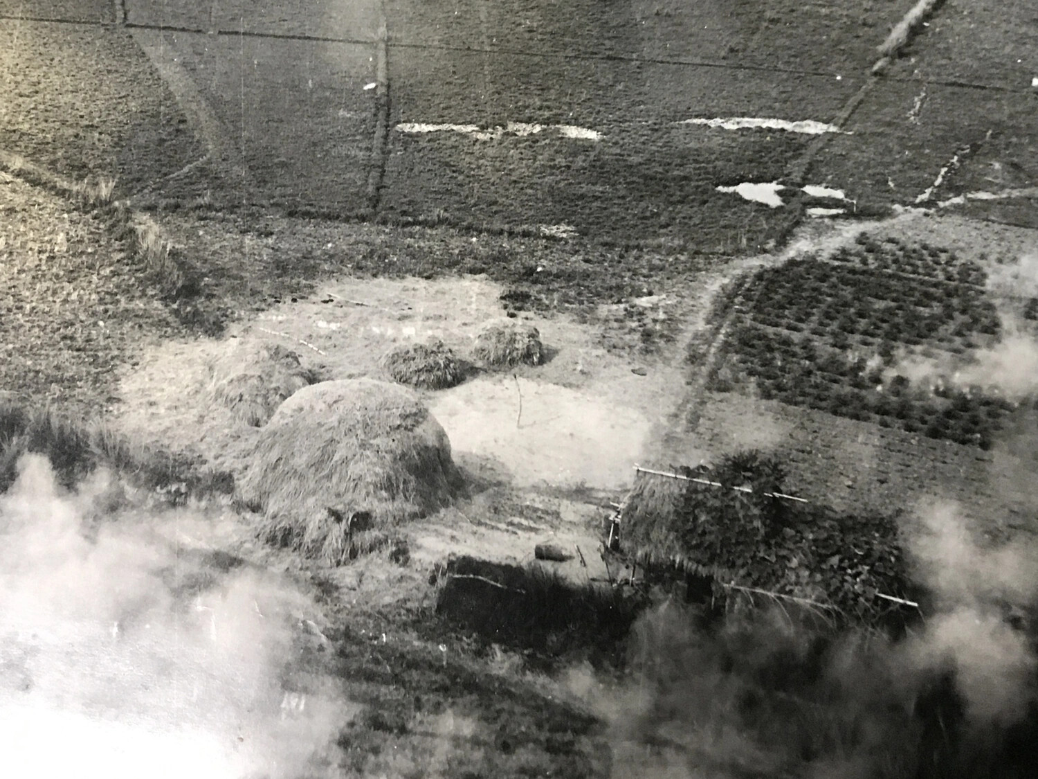 Low-Altitude Aerial View of Cultivated Fields, Haystacks, and Thatched Shelter Amid Attack Smoke