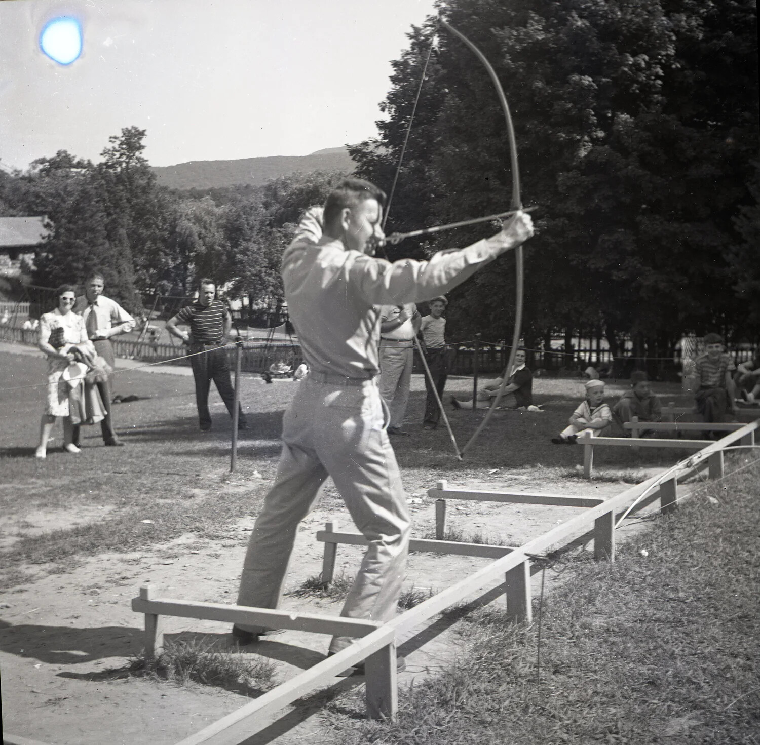 Archer Drawing a Longbow at an Outdoor Recreation Range, with Spectators