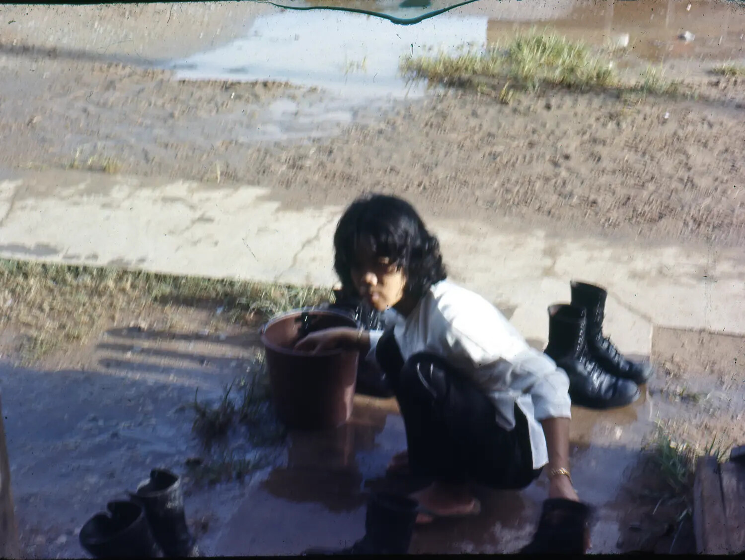 Vietnamese Civilian Drinking from Bucket Near Military Combat Boots, Vietnam War Era