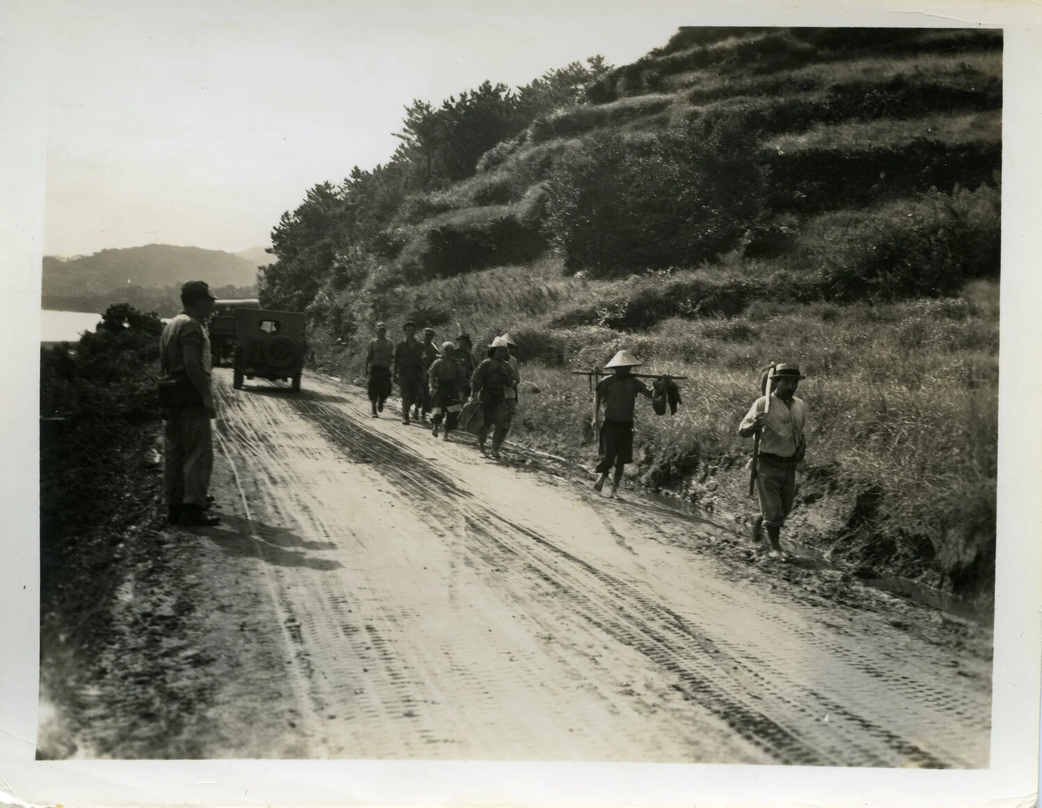 U.S. Serviceman Observing Okinawan Civilian Column on Coastal Road, Okinawa, 1945