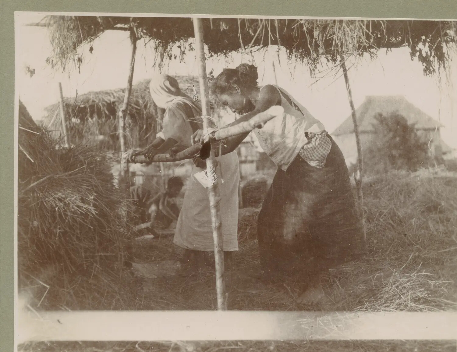 Two Women Processing Fiber or Grain Under Thatched Shelter, Philippines, c. 1890s-1900s
