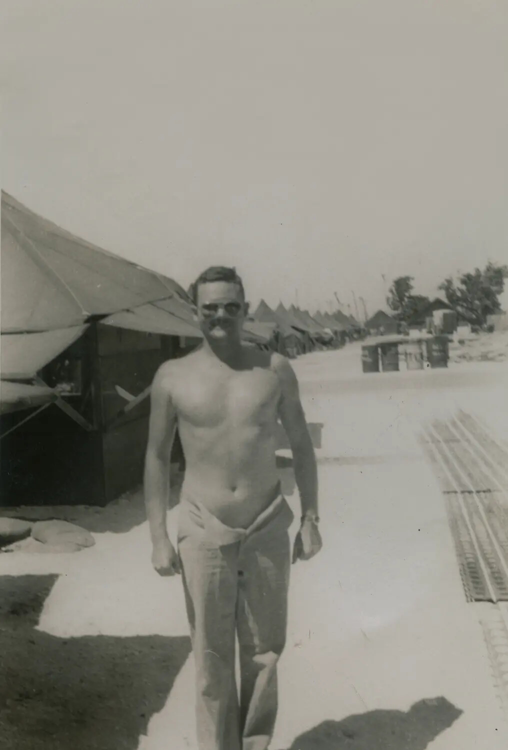 Shirtless Serviceman Walking Through Tent Camp with Marston Mat Stacks - WWII Photo Album