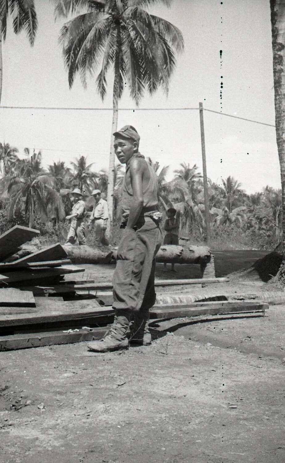 American Serviceman Beside Lumber Pile with Filipino Child in Background, Luzon, Philippines, WWII