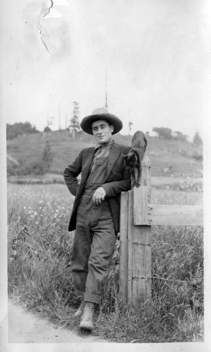 Young Man in Overalls Leaning on Fence Post with Cat, Rural Setting, Early 20th Century