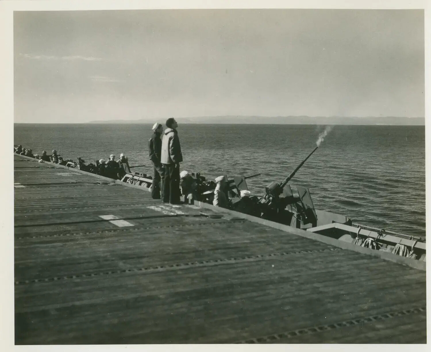 Anti-Aircraft Gun Crews Firing from Catwalk, USS Petrof Bay (CVE-80), with Coastline in Background