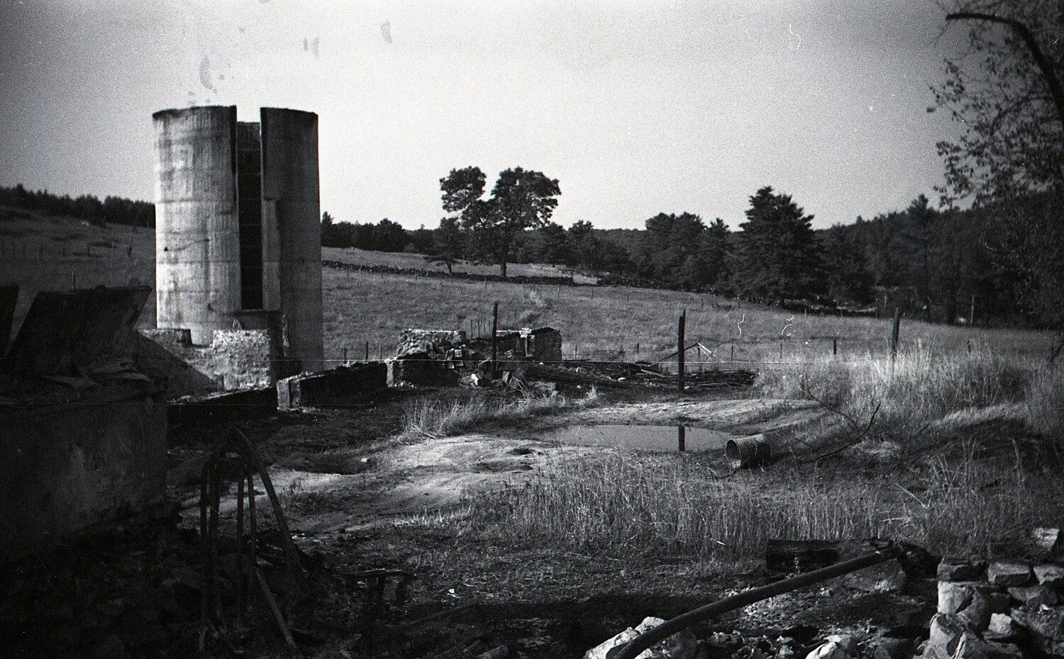 Surviving Concrete-Stave Silos Amid Dairy Barn Fire Ruins, Rural New England, c. 1940s