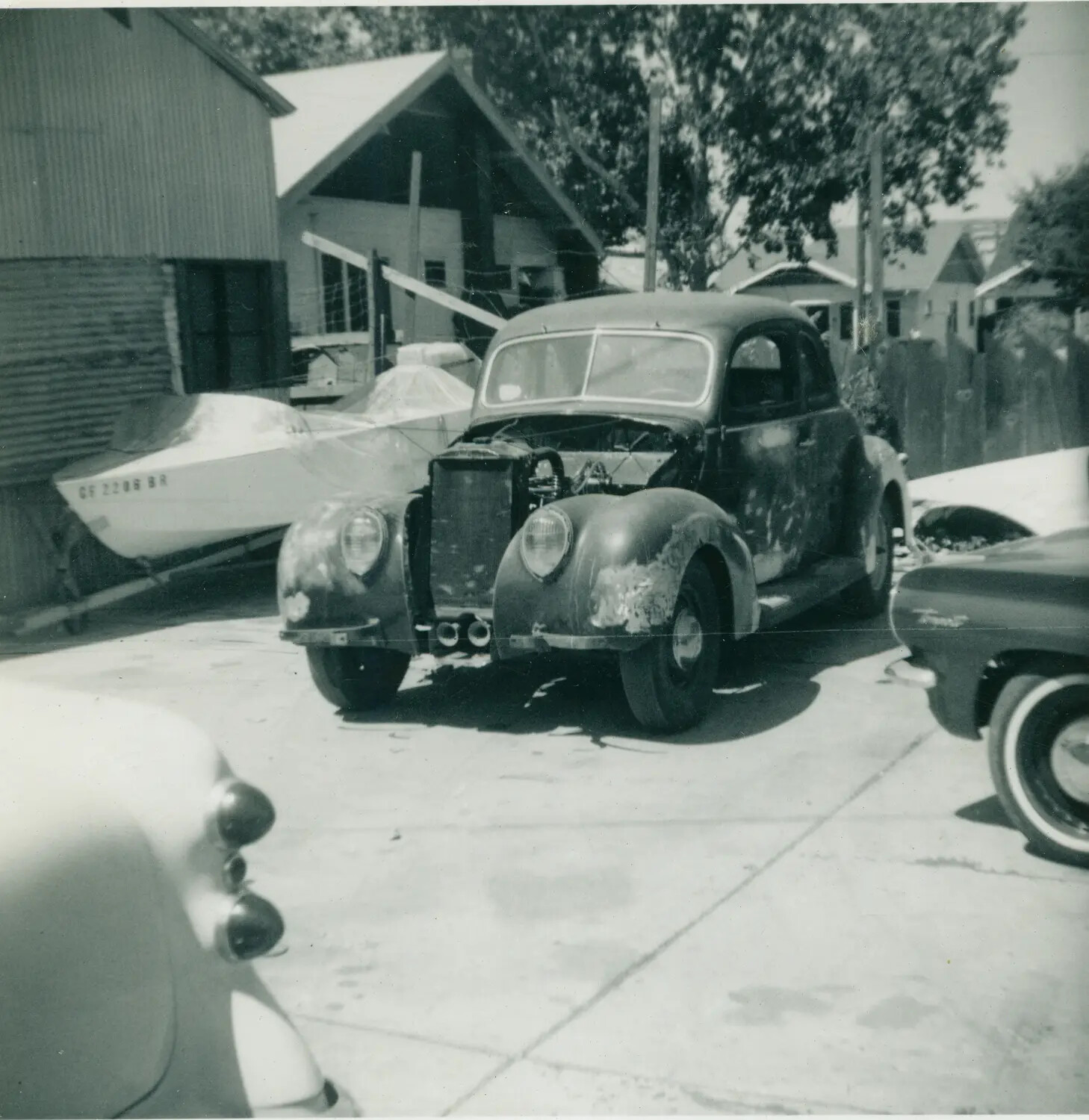 Civilian Snapshot: Vintage Automobile Restoration Project with Boat Trailer, Residential Driveway