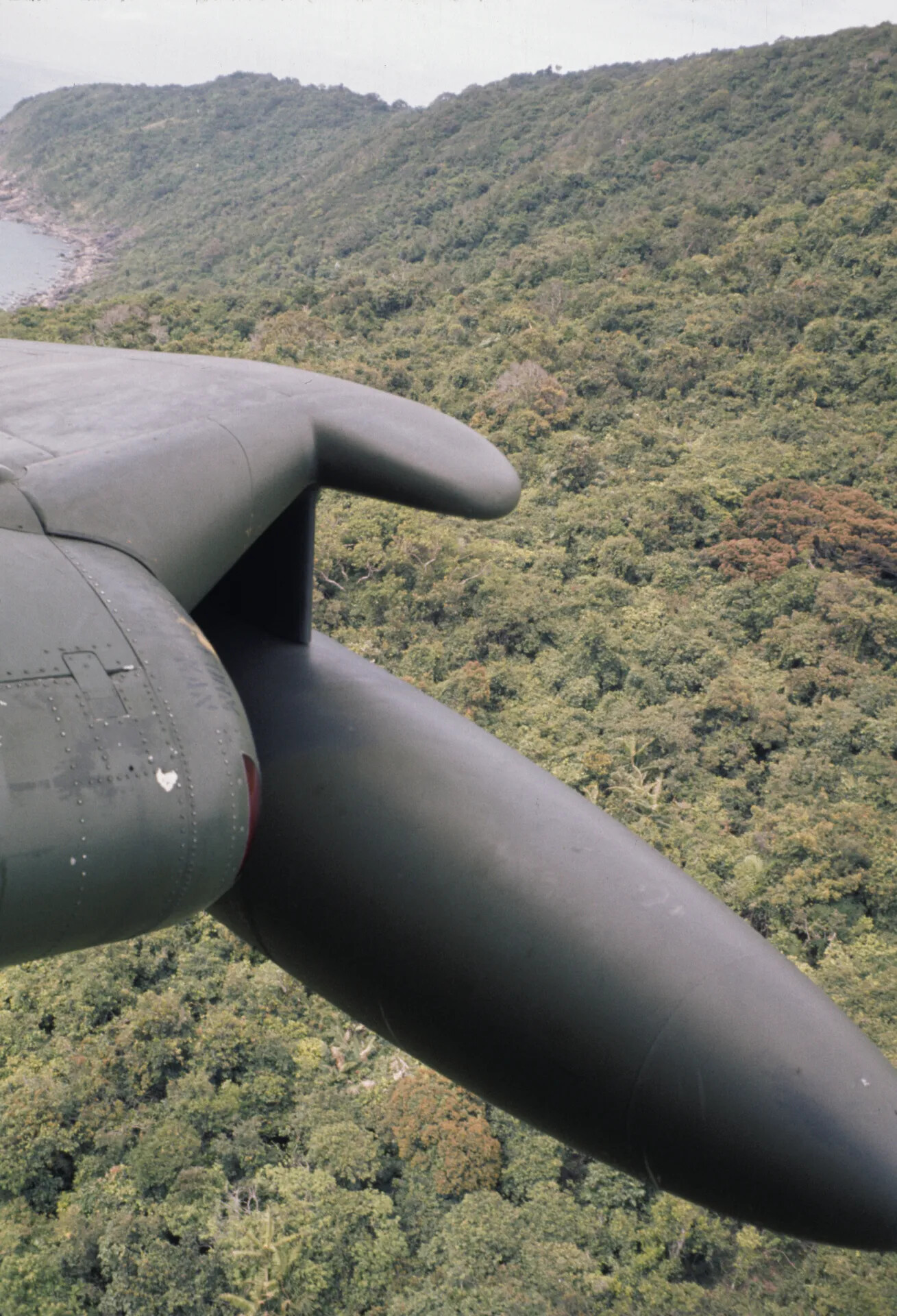Underwing External Fuel Tank and Wing of an A-1 Skyraider Over a Jungled Coastal Headland, Vietnam, circa June 1970