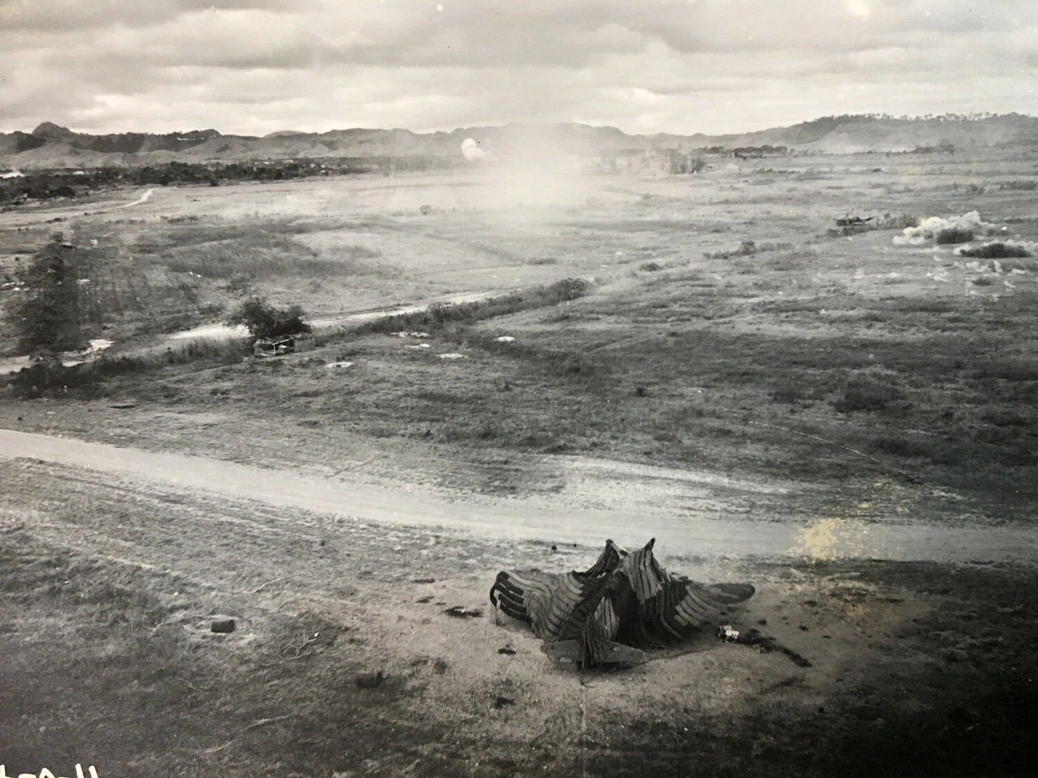Aircraft Wing Wreckage Beside Road with Distant Bomb Bursts
