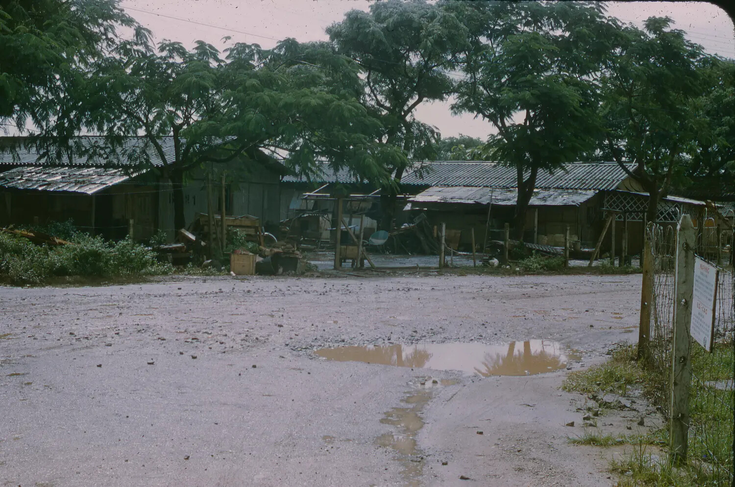 Rain-Soaked Compound Road with Tin-Roofed Support Buildings, South Vietnam, 1965