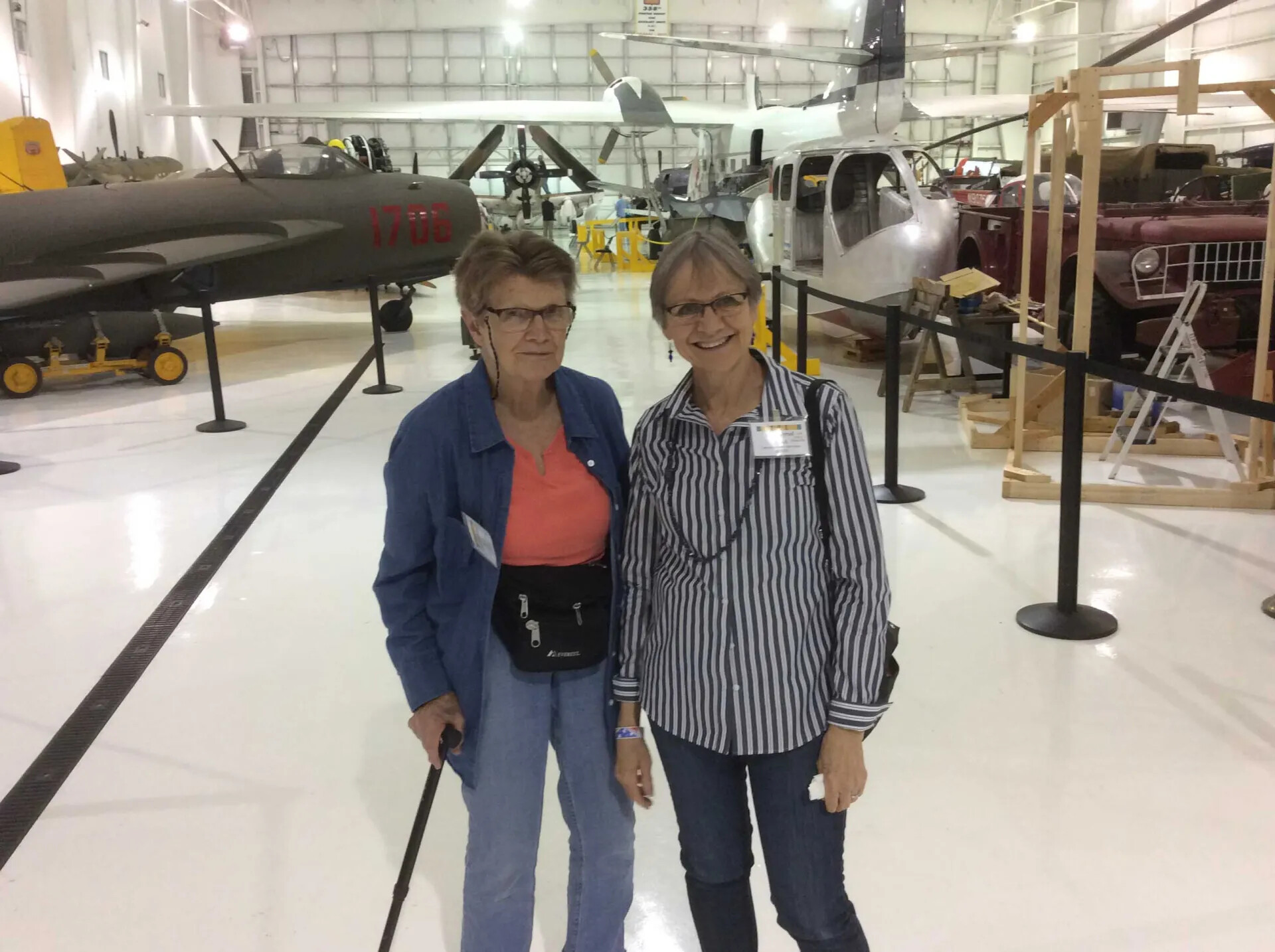 Two Visitors Posing Among Aircraft Under Restoration, Aviation Museum Hangar