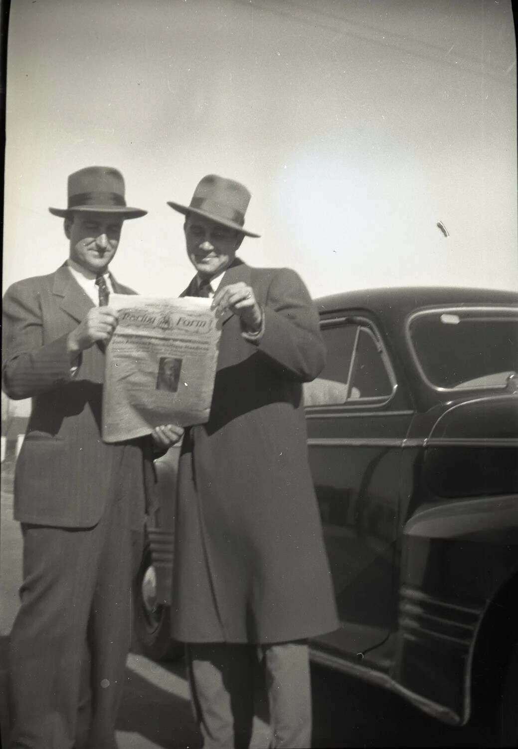 Two Men Displaying 'Racing Form' Newspaper Beside Sedan, Kelley Family Album