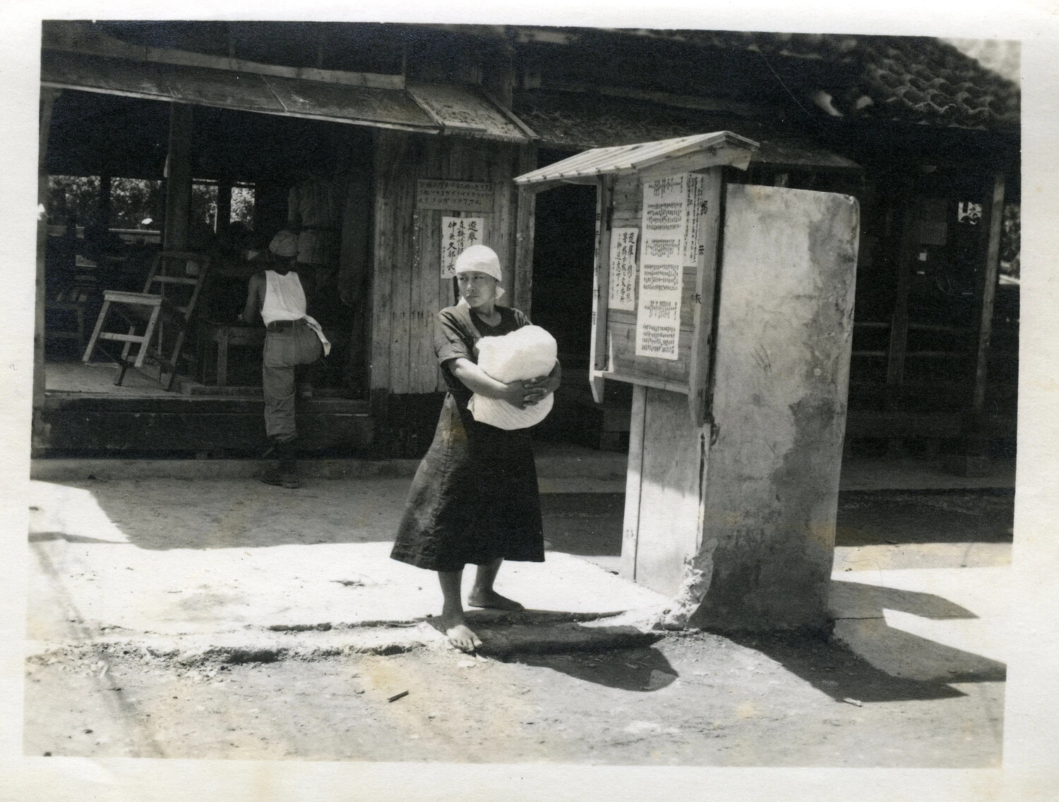 Okinawan Woman with Bundle Beside a Public Notice Board, Okinawa, WWII Era