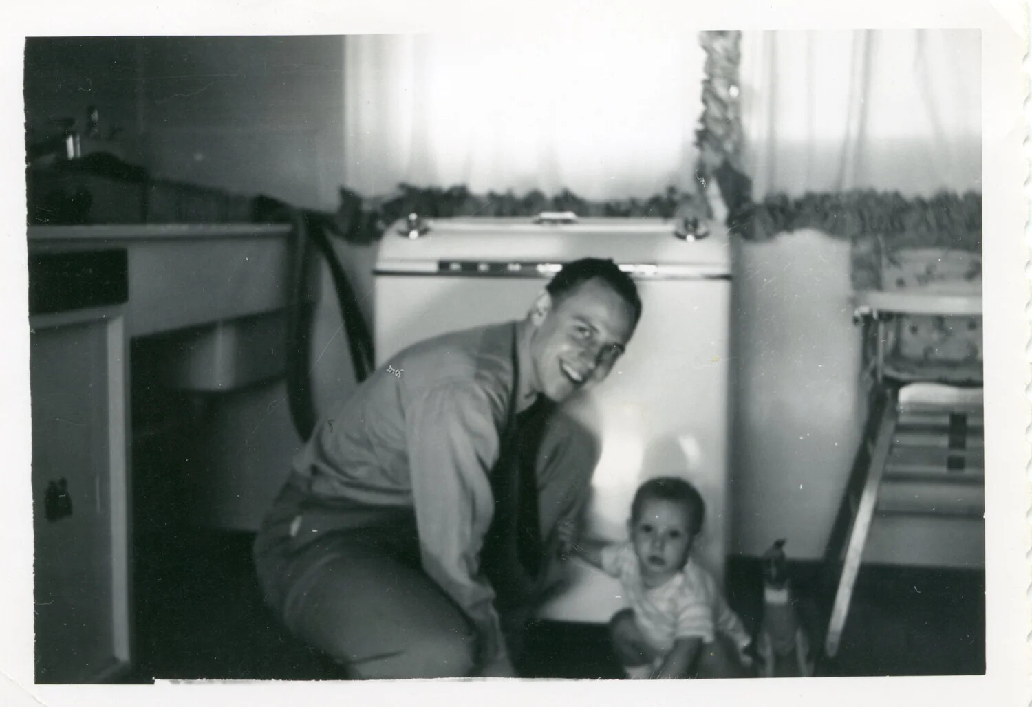 Man in Shirt and Tie with Toddler in Kitchen, Bancroft Family Album, Korean War Era