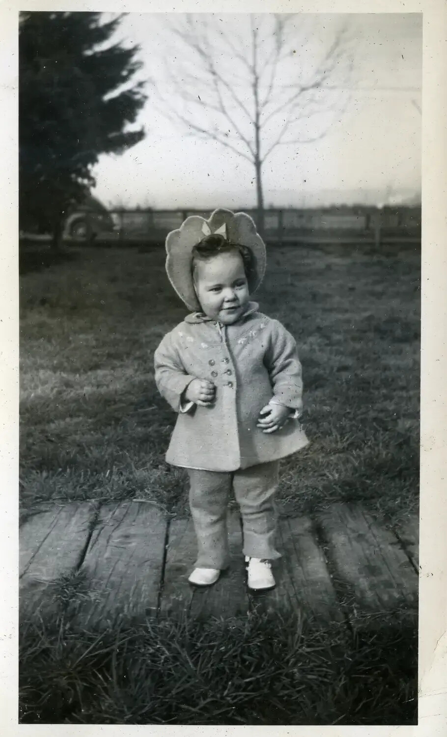Toddler in Bonnet and Coat Standing on Wooden Walkway, Family Snapshot (USS Maryland Album, 1930s-1940s)
