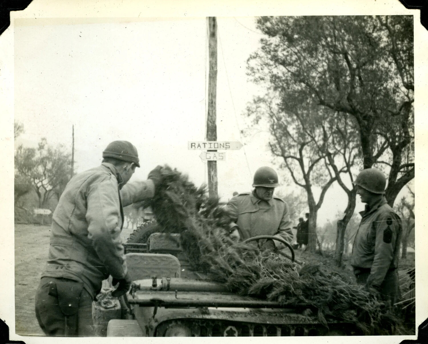 Soldiers Camouflaging a Jeep with Foliage Near Supply Signs, WWII European Theater