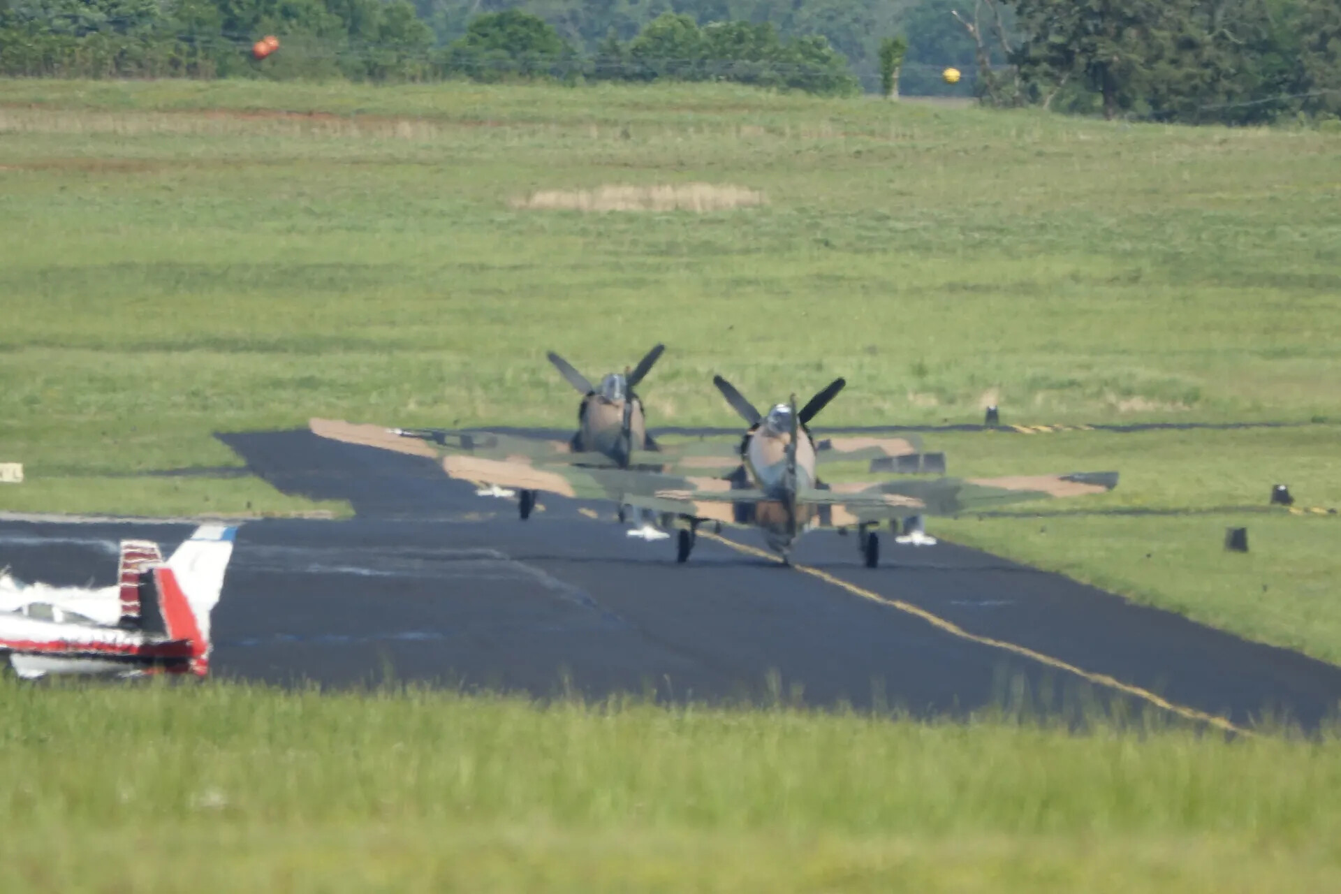 Two Camouflaged Douglas A-1 Skyraiders on Runway, with Parked Aircraft in Foreground, May 2019 Reunion Event