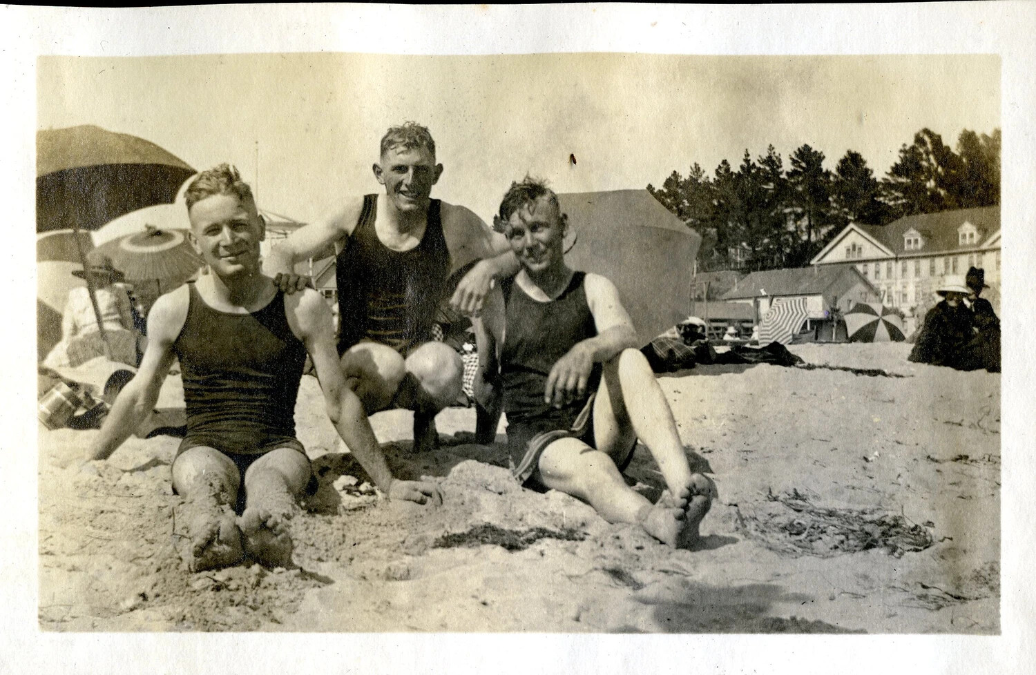 Three Young Men Posing Together at a Crowded Beach Resort, Early 20th Century