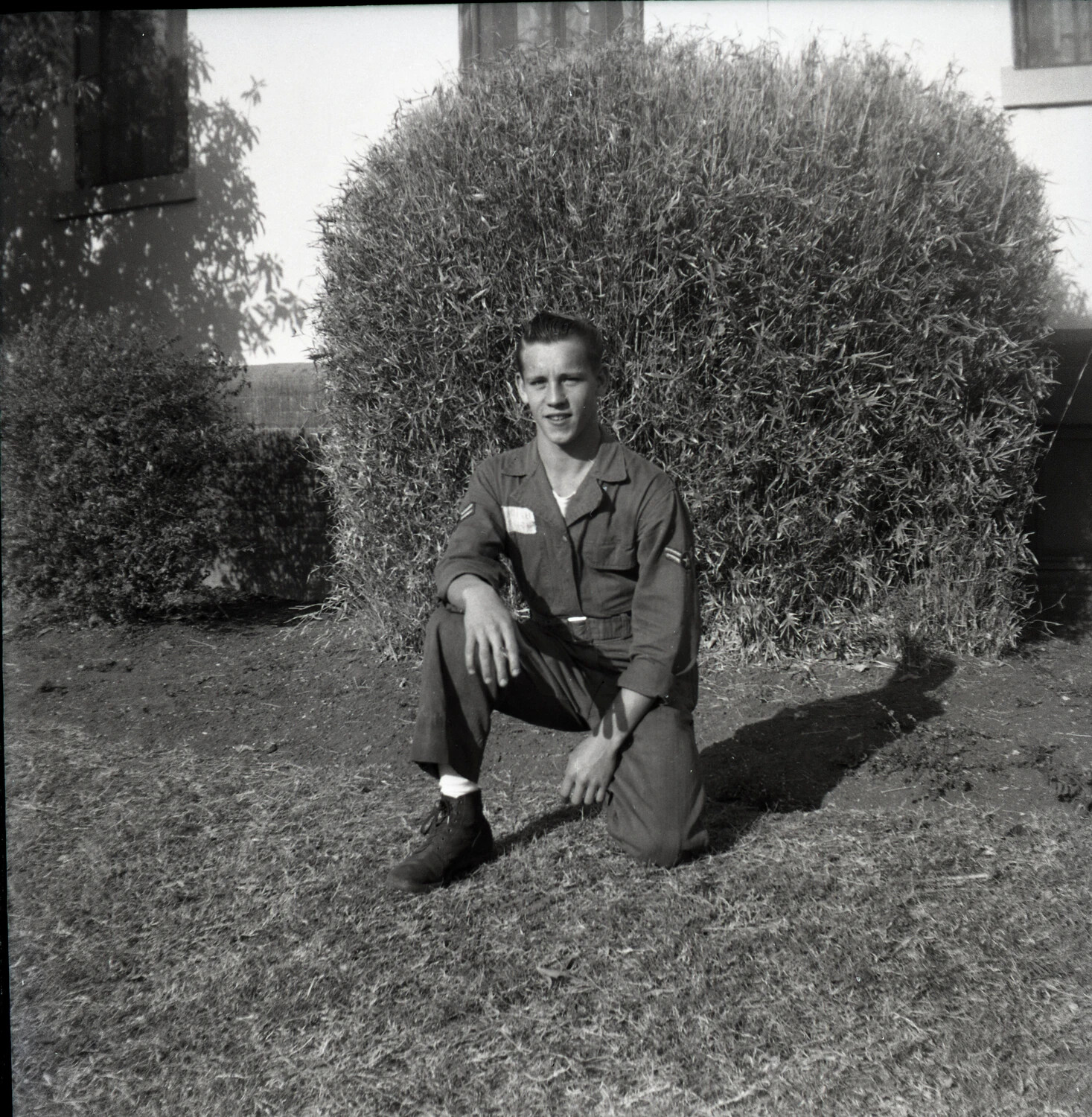 USAF Airman Kneeling for Portrait Before Hedge, Barracks Area, c. 1950s