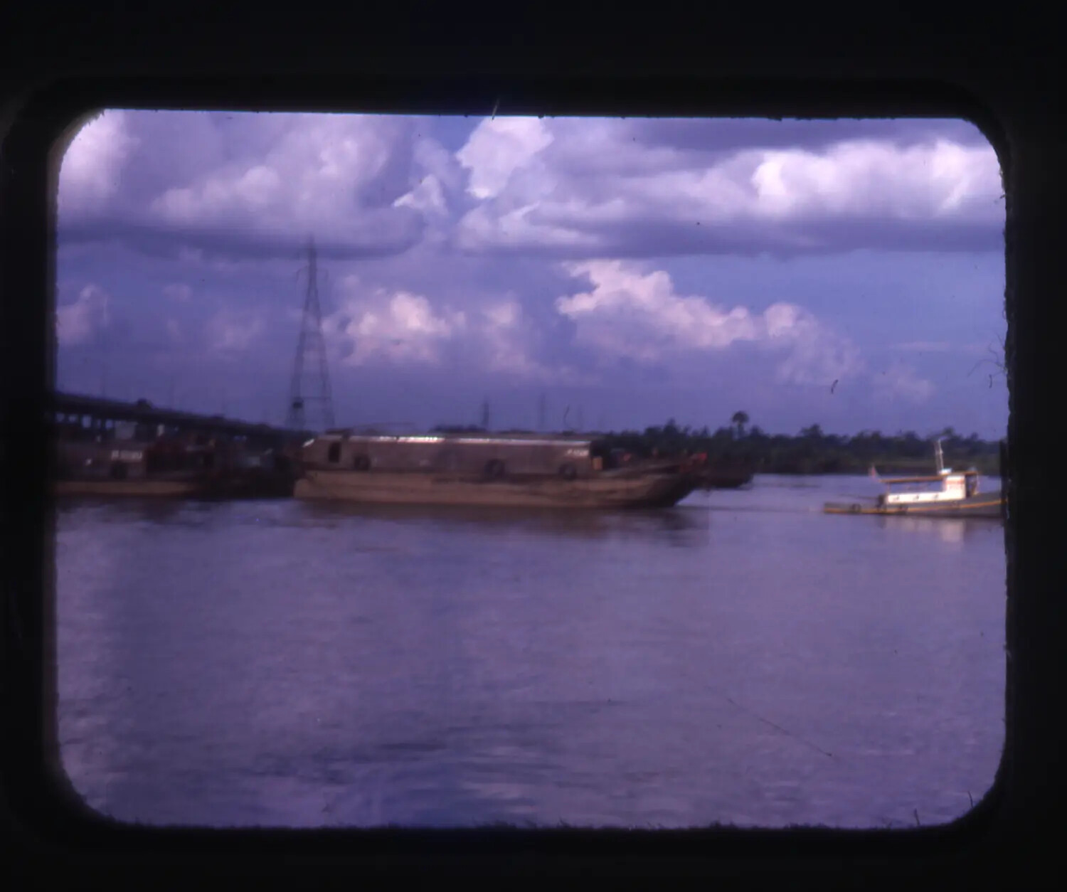 Barge Under Tow on Vietnamese River, with Bridge and Transmission Tower