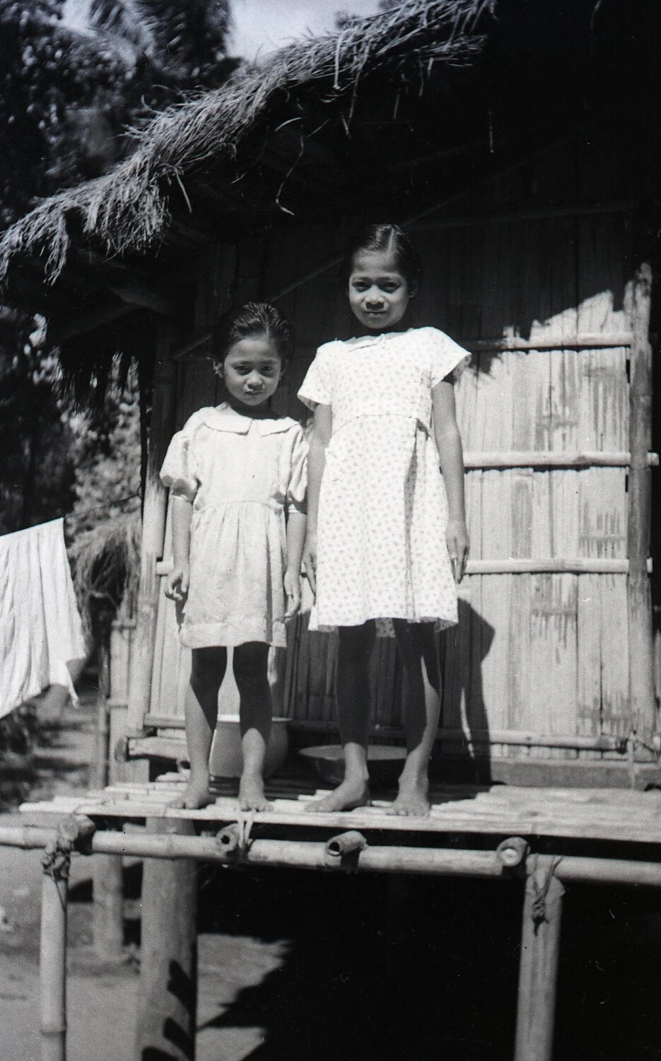 Two Filipino Girls on Bamboo Porch Under Thatched Roof, Luzon, Philippines, WWII Era
