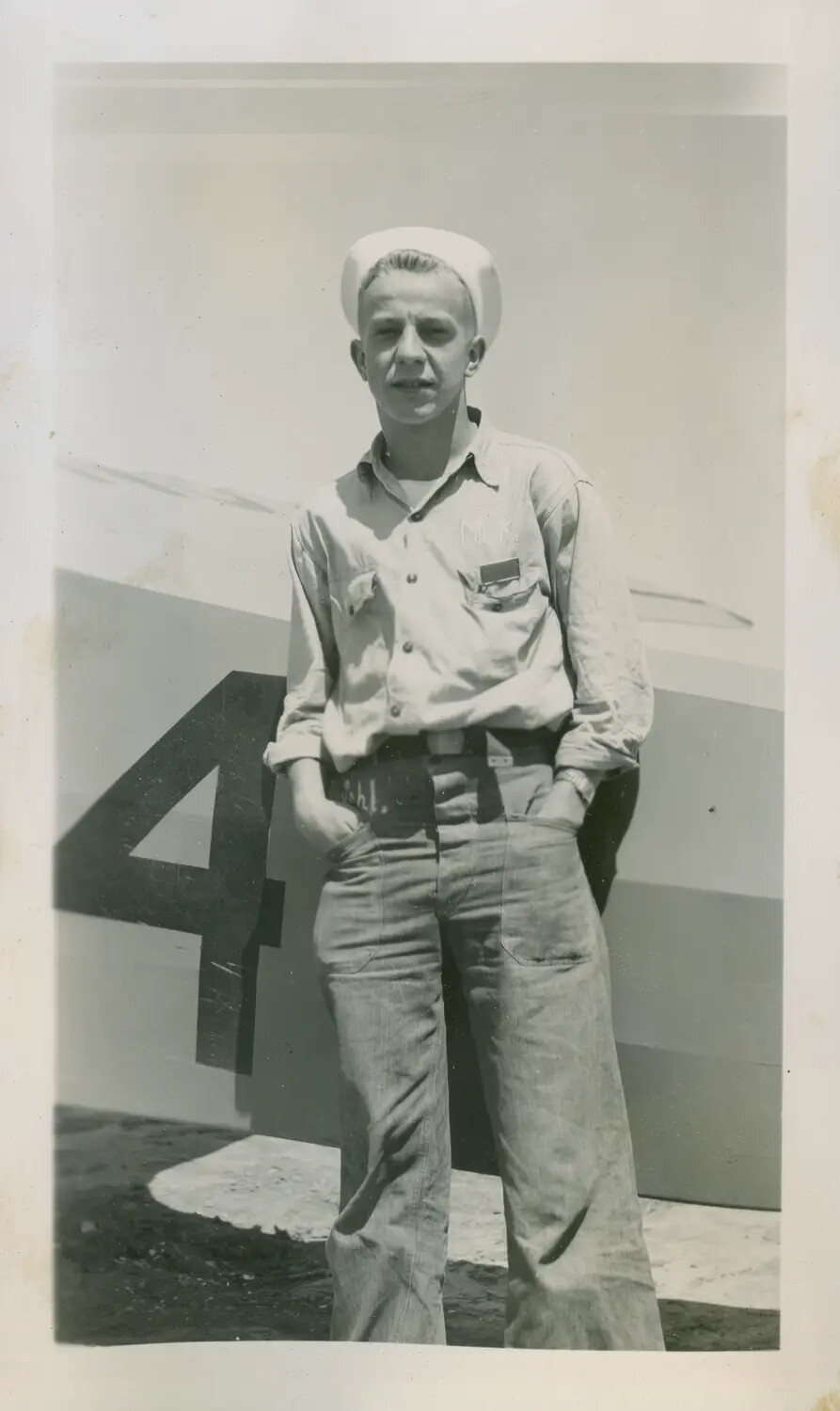Sailor Posed Before a Numbered Training Aircraft at a Naval Air Station