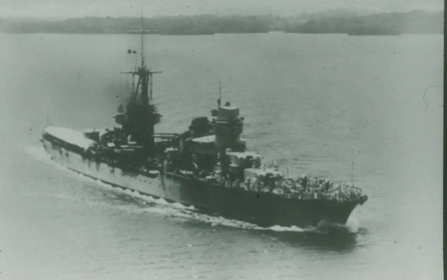 Aerial View of WWII-Era Warship Underway Near Coastline