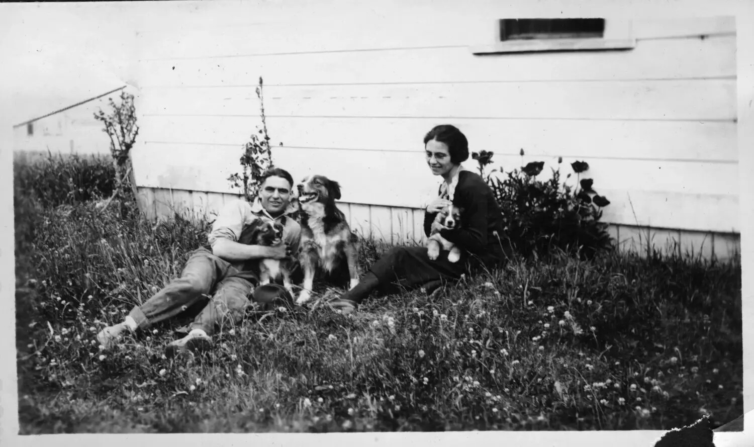 Couple Seated in Grass with Three Dogs Beside House, c. 1920s