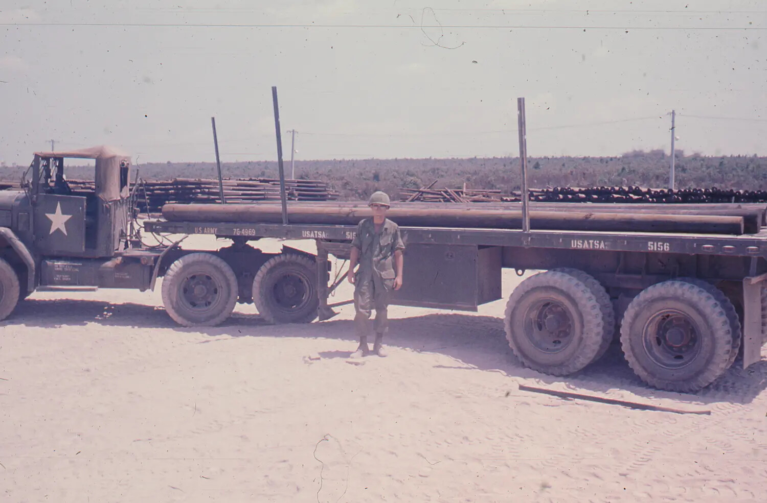 US Army Soldier Beside Flatbed Semi-Trailer Loaded with Pipe, Vietnam, 1968