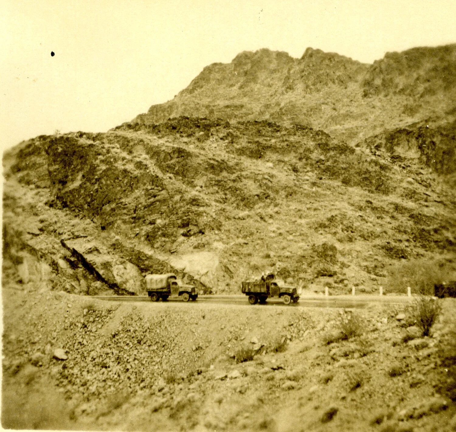 Two U.S. Army Trucks on a Mountain Road Through Arid Terrain, WWII Era