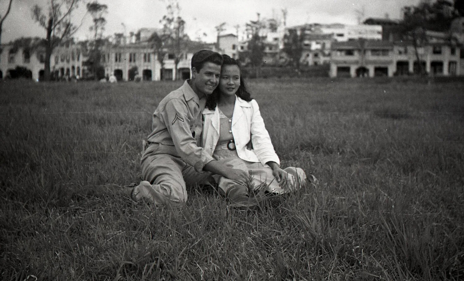 U.S. Soldier and Filipino Woman Seated in Field Before War-Damaged Buildings, Luzon, Philippines, WWII