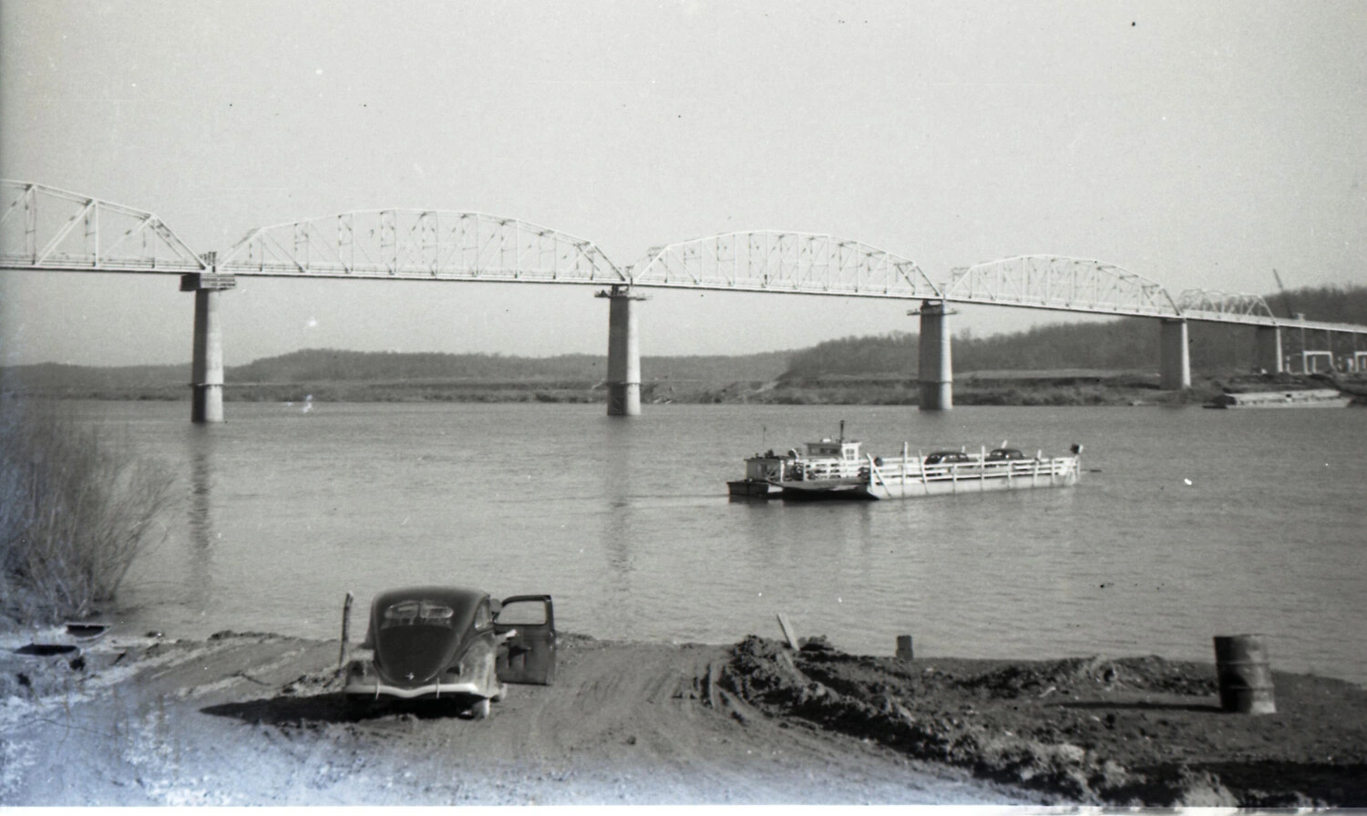River Crossing with Truss Bridge, Car Ferry, and Wrecked Volkswagen Beetle (Likely Misfiled, Non-WWII Image)