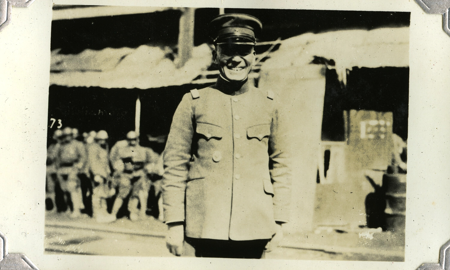 Smiling Military Officer in Service Uniform with Seated Troops in Background, Possibly Philippines, WWII Era